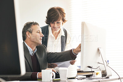 Buy stock photo Two colleagues using a computer in a modern office. A mature businessman and businesswoman working online, talking about business matters