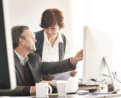 Buy stock photo Two colleagues using a computer in a modern office. A mature businessman and businesswoman working online, talking about business matters