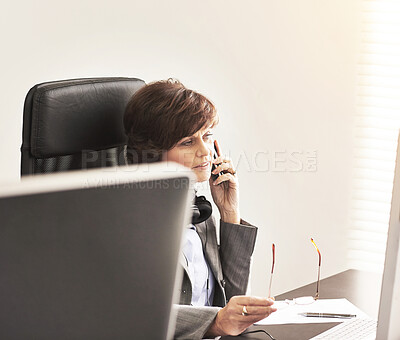 Buy stock photo A businesswoman using a phone to make a call in a modern office. A mature female executive talking on her smartphone browsing online with a computer for business