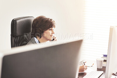 Buy stock photo A businesswoman using a phone to make a call in a modern office. A mature female executive talking on her smartphone browsing online with a computer for business