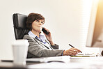 A businesswoman using a phone to make a call in a modern office. A mature female executive talking on her smartphone browsing online with a computer for business