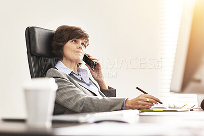 Buy stock photo A businesswoman using a phone to make a call in a modern office. A mature female executive talking on her smartphone browsing online with a computer for business