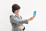 A businesswoman using a phone, isolated on a white background. A mature female executive browsing online for business and taking a selfie with her smartphone in an office or studio