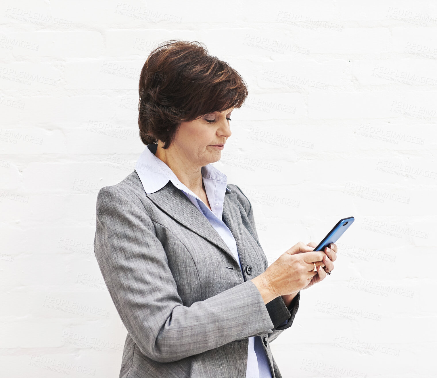 Buy stock photo A businesswoman using a phone, isolated on a white background. A mature female executive browsing online for business with her smartphone in an office or studio