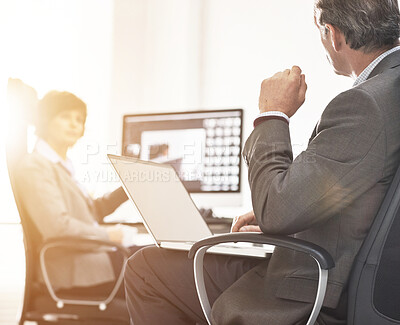 Buy stock photo Two colleagues using a laptop in a modern office. A mature businessman and businesswoman working online with a computer, talking about business matters