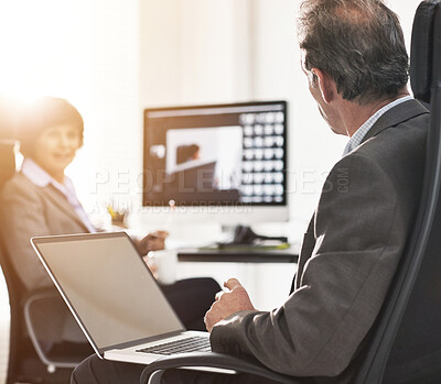 Buy stock photo Two colleagues using a laptop in a modern office. A mature businessman and businesswoman working online with a computer, talking about business matters