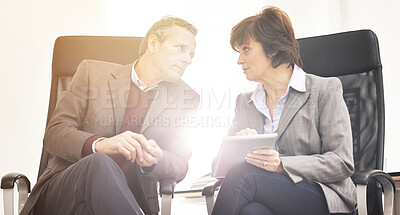 Buy stock photo Two colleagues using a tablet in a modern office. A mature businessman and businesswoman working online with a touchscreen, talking about business matters