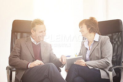 Buy stock photo Two colleagues using a tablet in a modern office. A mature businessman and businesswoman working online with a touchscreen, talking about business matters