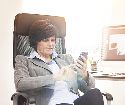 Buy stock photo A businesswoman using a phone in a modern office. A mature female executive browsing online for business with her smartphone at work