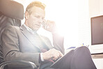 A businessman using a phone to make a call in a modern office. A mature male executive talking on his smartphone and working online with a digital tablet for business