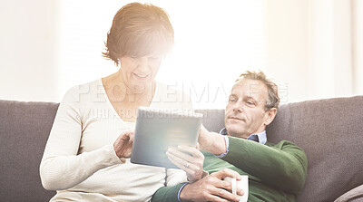 Buy stock photo A mature couple using a digital tablet, relaxing at home. A happy senior man and woman in love browsing online with a touchscreen on the couch