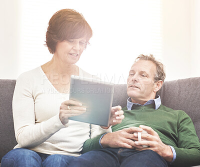 Buy stock photo A mature couple using a digital tablet, relaxing at home. A happy senior man and woman in love browsing online with a touchscreen on the couch