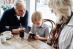 Family, grandparents and kid with phone at cafe for online games, e learning and streaming video together. Senior people with boy child at coffee shop and mobile for chat or reading restaurant menu