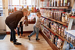 Child, man and woman in candy shop with jar for gift, shopping or choice with love, care or bonding. Grandparents, boy kid and retail store with container for sweets, decision or present with family
