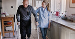 Nurse help senior man in crutches in home kitchen, medical rehabilitation and recovery. Caregiver, person with a disability walk and support, health and physiotherapy, healing injury or accident pain