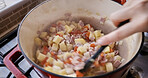 Person, hand and food cooking closeup on stove pot for health nutrition meal, vegetables or potato. Finger, spoon and mix on gas device for dinner eating or home recipe for stew, protein or hungry