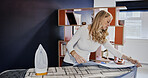 Housewife, iron and laundry on board in living room by cleaning, washing or household chore. Woman, looking or satisfaction for placement of garment, shirt or linen for ironing, neat or fresh in home