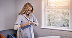 Woman, wear clothes and iron in house, laundry and housework in living room, apartment or home. Housekeeping service, chores and person with fresh shirt, maid cleaning and domestic work for hygiene