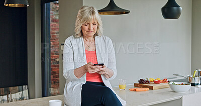 Buy stock photo Old woman in kitchen, relax with phone and cooking on calm morning, sitting on counter and checking social media. Home, breakfast salad and senior person with smartphone, networking and communication