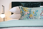 Bed, pillow with floral design and hotel room for hospitality, accommodation for comfort with furniture and decor. Bedroom, property or house for vacation, getaway or luxury resort with closeup