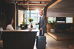 Travel, reception and mature man with suitcase in hotel for business meeting, hospitality or check in. Service, concierge woman and person with luggage for welcome, vacation or sales convention
