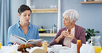 Senior woman, caregiver and book at breakfast, listen or bonding with food, retirement or help in home. People, connection and literature in morning with care, storytelling or support at family house