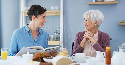 Buy stock photo Elderly woman, caregiver and reading book in home, breakfast or smile in retirement in dining room. People, connection and literature in morning for care, storytelling and support with novel in house