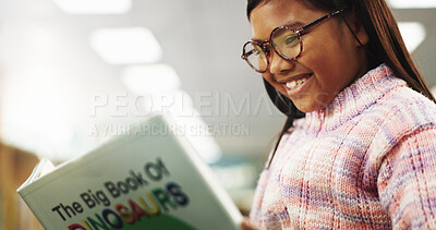 Buy stock photo Girl, child and happy with reading book at library for education, learning or glasses for dinosaur story. School kid, smile and scholarship for language, knowledge or study for development at academy
