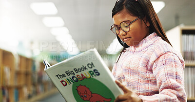 Buy stock photo Girl, child and reading with book at library for development, learning and glasses with dinosaur story. School kid, smile and scholarship with language, knowledge and study for education at academy