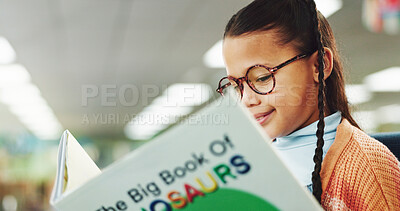 Buy stock photo Girl, child and smile with reading book at library for education, learning or glasses for dinosaur story. School kid, happy and scholarship for language, knowledge or study for development at academy