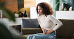 Sofa, woman and hands on stomach for pain, menstrual cycle and endometriosis in living room at home. House, female person and closeup with abdomen ache for constipation, gastro crisis or period cramp
