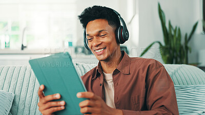 Buy stock photo Headphones, tablet and man on sofa in home listening to music, album or playlist for review. Happy, relax and male person with technology and audio tech for streaming app with podcast in apartment.
