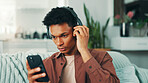 Headphones, phone and man on sofa in home listening to music, album or playlist for review. Serious, confused and male person with cellphone and audio tech for streaming app with podcast in apartment