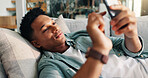 Man, relax and scroll with phone on sofa for weekend break, dating site chat and app download. Smile, person and rest with smartphone in home with online subscription, social media post or web search