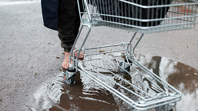 Buy stock photo Homeless, person and walking with shopping cart in street for poverty, economic hardship or vulnerability. Barefoot, beggar and trolley in rain puddle for welfare crisis, struggle or social injustice