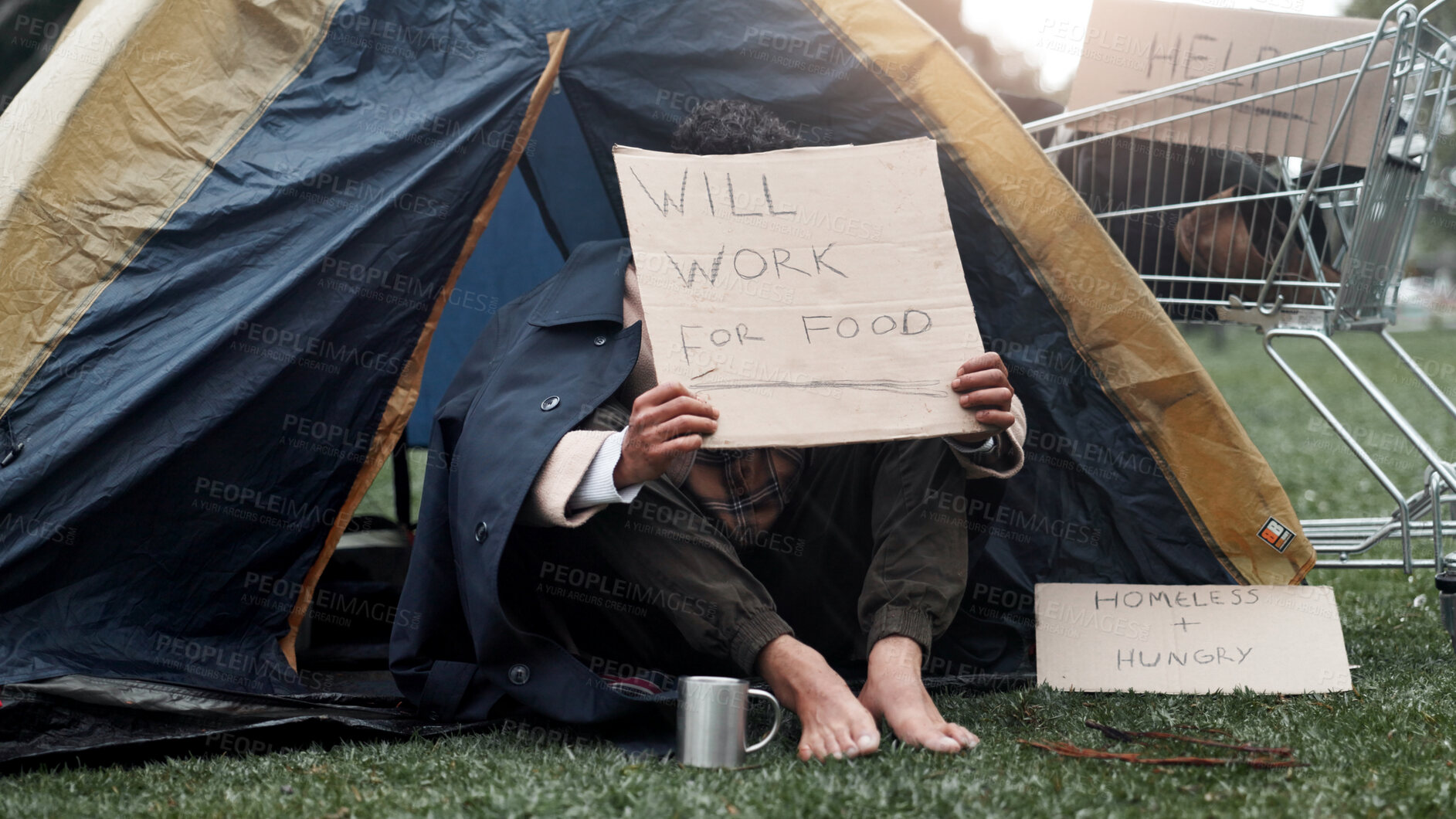 Buy stock photo Person, homeless and cardboard for begging with cup, poverty and ask for job, change and food at park. Feet, outdoor and poster for donation, care and hungry on ground with hope for work opportunity