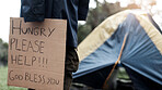 Person, homeless and hungry with cardboard for begging by tent, poverty or ask for food at park. Sign, outdoor and poster for donation, care and need for kindness with hope for charity meal in winter