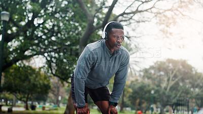 Buy stock photo Fitness, man and tired with headphones at park for running fatigue, workout recovery and cardio challenge. Athlete, black person and resting in nature with breathing break, exercise music and podcast
