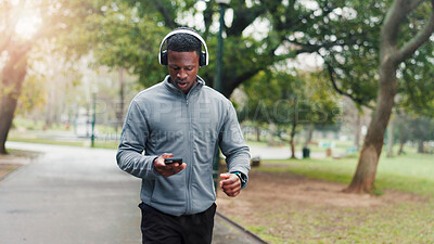 Buy stock photo Fitness, man and phone with headphones at park for music streaming, check running statistics or monitor progress. Black person, athlete and mobile app for playlist, workout podcast and training audio
