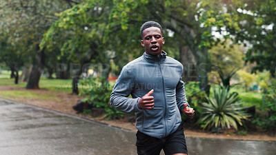 Buy stock photo Running, rain and man with fitness at park for marathon exercise, endurance or discipline with cardio workout. Black person, wellness and runner with breathing, sports challenge and practice in road