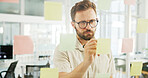 Creative, man and writing on sticky notes by glass wall for campaign planning, budget development and ideas. Marketing manager, employee and calendar tasks for project management or business strategy