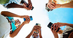 Below, hands and people with cellphone, outdoor and smile with connection, social media or group. Blue sky, low angle or friends with closeup, smartphone or tech for message, texting or communication