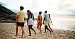 Back view, holiday and friends walking on beach for vacation or summer trip on tropical island together at sunset. Group, tourism and people at ocean for relax, bonding and travel on adventure at sea