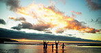 Sunset, freedom and friends in sea water for holiday, vacation and summer trip on tropical island. Group, ocean and people in celebration by beach for travel, adventure and hands up together at dusk