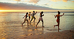 Sunset, running and friends in sea water for holiday, vacation and summer trip on tropical island. Group, ocean and people race by beach with energy for freedom, travel and excited for adventure