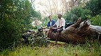 Happy men, friends and break with log at forest for hiking, journey or adventure together in nature. Male people, rest or snack on tree stump with food for trekking stop, trip or outdoor exploration