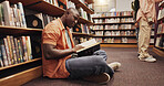 Black man, reading book and floor in library for literature, research and studying for knowledge. Person, student and novel with academic information, scholarship and learning of education assignment