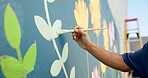Man, hand and painting in city for wall art, creative mural and project to uplift community. Volunteer, creativity and outdoor with equipment for floral decor, social responsibility and DIY hobby