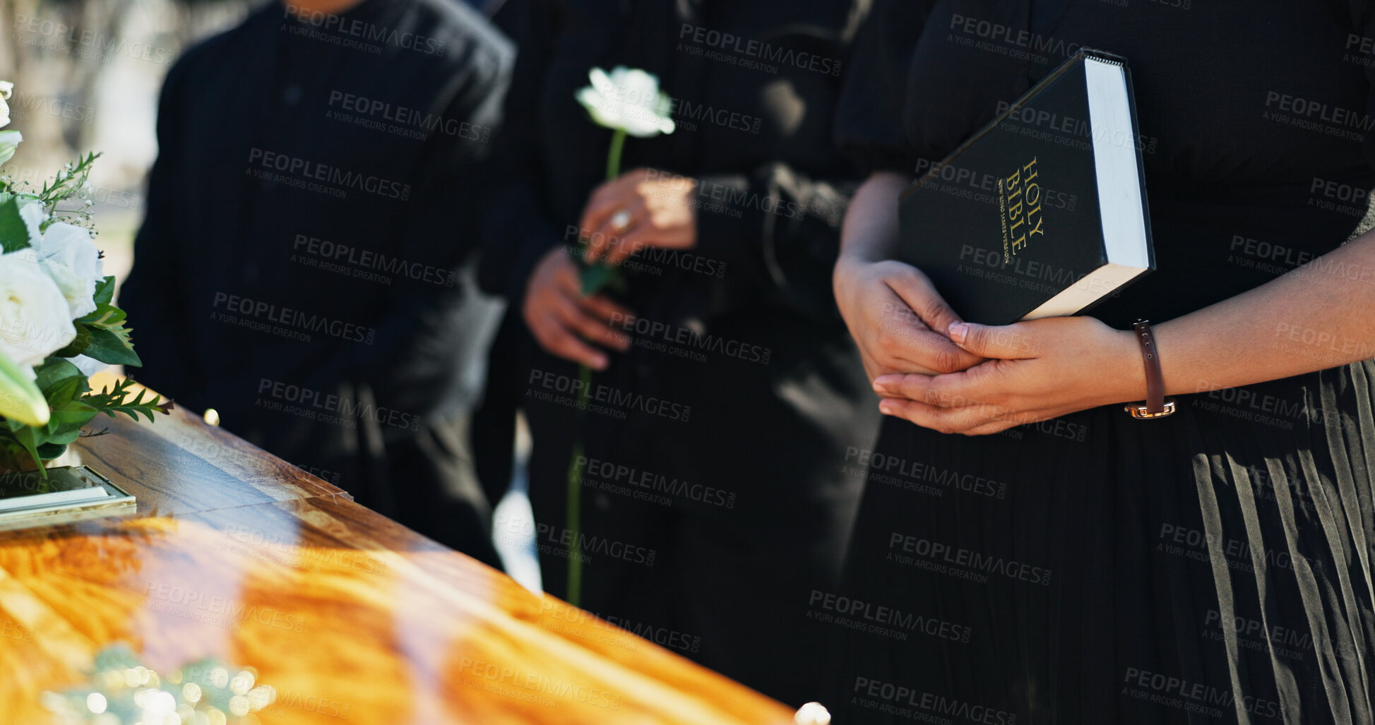 Buy stock photo Bible, hands and people by coffin at funeral for respect, blessing or spiritual comfort at graveyard. Religion, prayer and family by casket with holy book for grief, loss or farewell at burial.