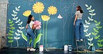 Women, talking or friends painting on wall for mural, drawing flowers or community service at building. Artist, creative or girls with teamwork for floral decoration, renovation or project for design